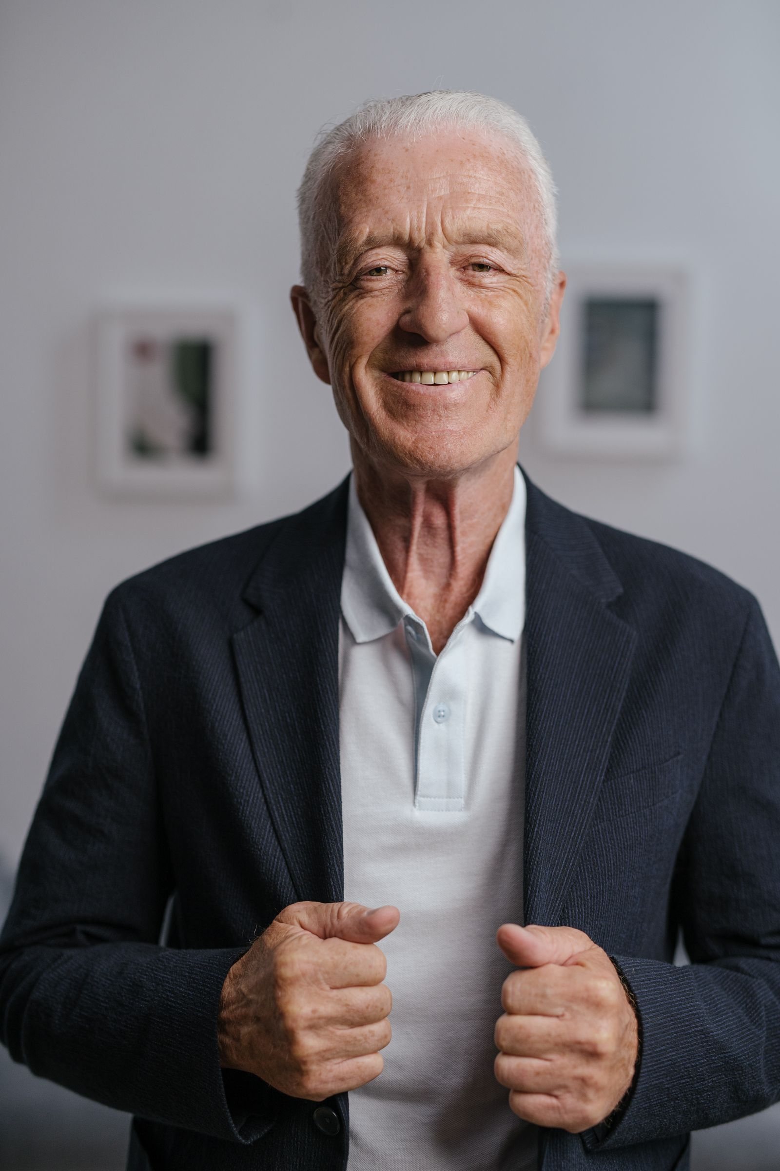 Portrait d’un homme aux cheveux blancs, veste sombre, sur fond neutre.